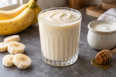 Smoothie banane yaourt crémeux dans un verre, avec des rondelles de banane et du yaourt nature.